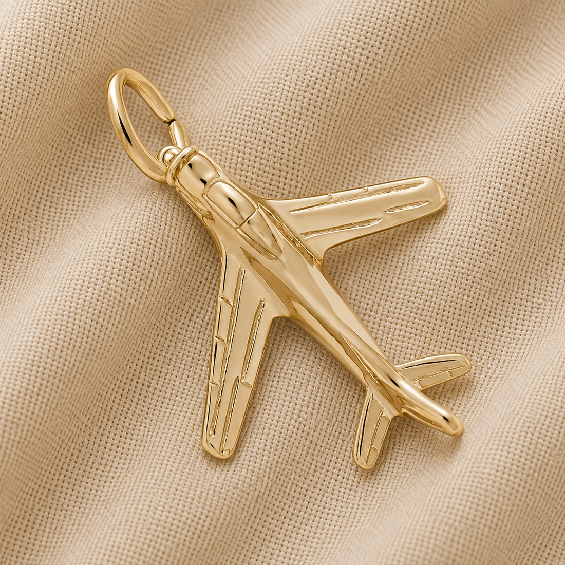 A gold-plated Military Airplane Charm by Rembrandt Charms rests on a beige, textured fabric background, making it a striking piece of aviation jewelry.