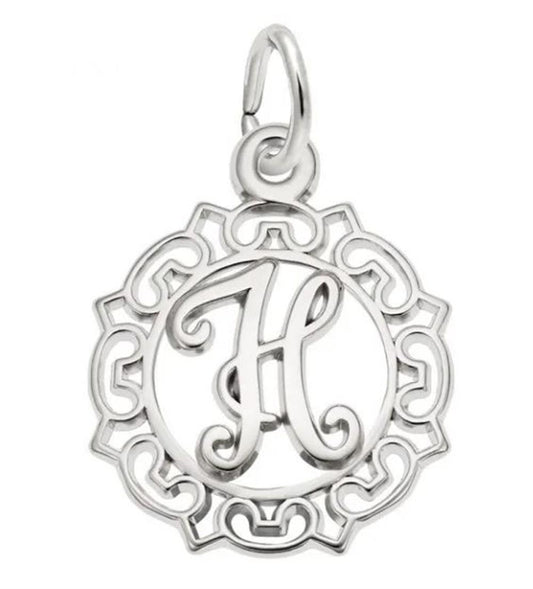 The Ornate Letter "H" Charm from Rembrandt Charms is crafted in sterling silver and showcases an intricately designed border with a circular motif. Inside the circle, a prominent, stylized letter "H" stands out, creating an exquisite charm. At the top of the pendant is a loop for easy attachment to a chain or bracelet.