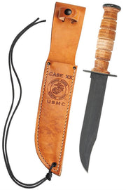 The USMC BROWN LEATHER HUNTER MARINE KNIFE by W.R. Case & Sons Cutlery Co., featuring a leather handle and black blade, sits next to its brown leather sheath. The sheath is distinguished by embossed text and a logo, with a black cord attached at the top.