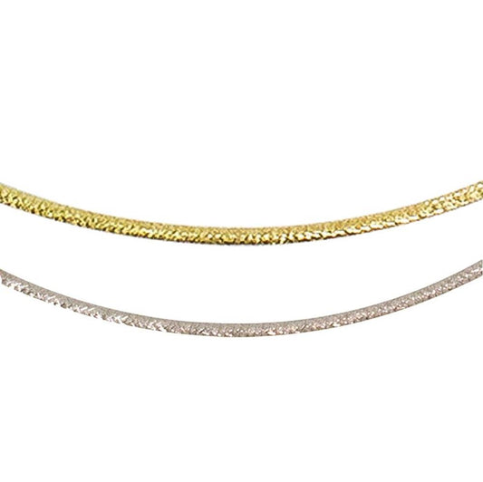 Close-up image of two elegant chains. The top chain, a Bellarri 14kt Reversible Omega Chain in 14KW / 14KY with a length of 17" and a 2" extender, showcases its gold hue, while the bottom chain gleams in silver. Both chains feature a textured surface that reflects light beautifully, giving them a shimmering appearance. The background is plain white.