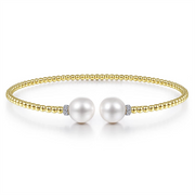 A 14K Yellow Gold Bujukan Diamond and Pearl Split Bangle from Gabriel & Co, featuring two large cultured pearls at the center, separated by small diamond accents. This gold beaded bracelet has a simple, elegant design and is shown against a white background.