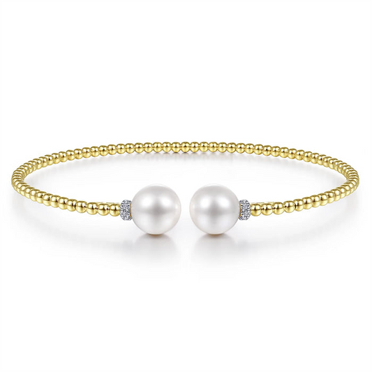 A 14K Yellow Gold Bujukan Diamond and Pearl Split Bangle from Gabriel & Co, featuring two large cultured pearls at the center, separated by small diamond accents. This gold beaded bracelet has a simple, elegant design and is shown against a white background.