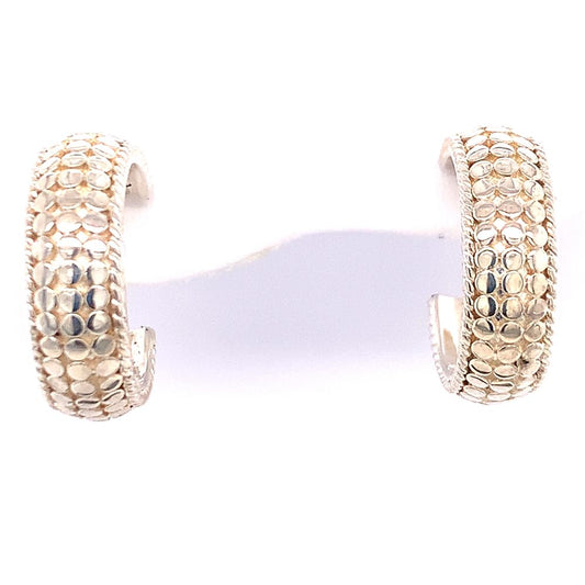 The Sterling Silver Dome Hoop Earrings from Anna Beck Designs feature a gold-tone dome shape with a pebble-like pattern. The wide-band design showcases intricate, shimmering details that reflect light beautifully. Presented on a white background, these earrings highlight sterling silver accents that add an extra touch of elegance.