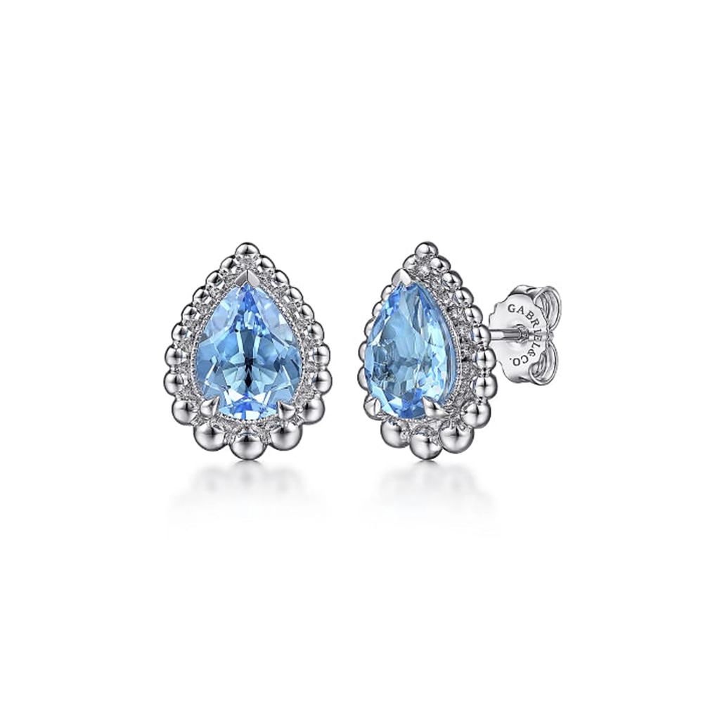 Introducing the Gabriel & Co 925 Sterling Silver Faceted Swiss Blue Topaz Pear Shape Bujukan Stud earrings. These stunning Boutique Silver earrings feature prominent, teardrop-shaped Swiss Blue Topaz gemstones at their center. The gemstones are elegantly encircled by small, round silver details, enhancing their detailed and ornate appearance. Visible sterling silver earring backs with the Gabriel & Co brand marking complete this exquisite pair.