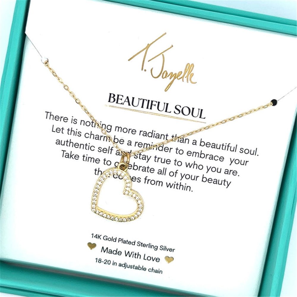 The T Jazelle Beautiful Soul Gold Charm Necklace features a heart-shaped pendant with crystals, presented in a turquoise box. Inside, a card reads “Beautiful Soul” and encourages you to embrace your beauty and stay true to yourself.
