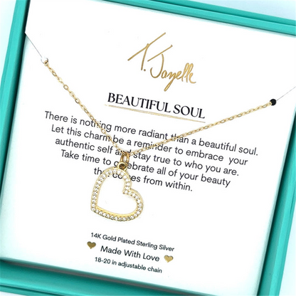 The T Jazelle Beautiful Soul Gold Charm Necklace features a gold heart pendant, displayed in a teal box with a “Beautiful Soul” card and an inspiring inner beauty message. The necklace rests elegantly above the printed text.