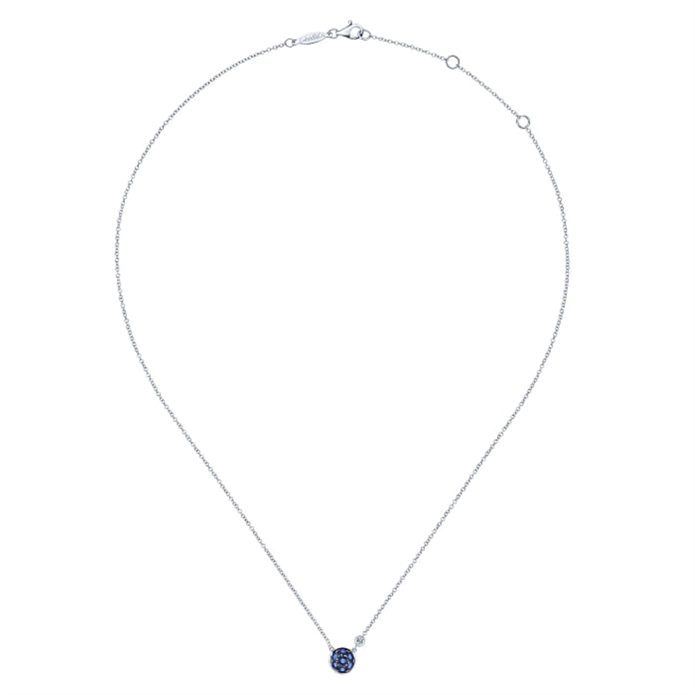 This delicate sterling silver necklace, part of Gabriel & Co's Lusso Color Collection, features a centrally positioned circular blue sapphire cluster and diamond pendant. The fine chain is elegantly adorned with small blue gemstones, with visible clasp and chain adjustment loops at the top.
