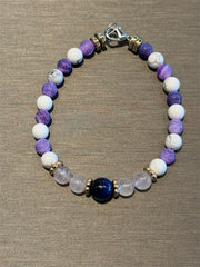 Redemption Jewelry’s B005 bracelet features Blue Tigers Eye, rose quartz, howlite, and frosted dragon agate beads, accented by a silver clasp and arranged on a gray surface.