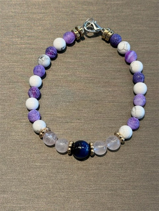 Redemption Jewelry’s B005 bracelet features Blue Tigers Eye, rose quartz, howlite, and frosted dragon agate beads, accented by a silver clasp and arranged on a gray surface.