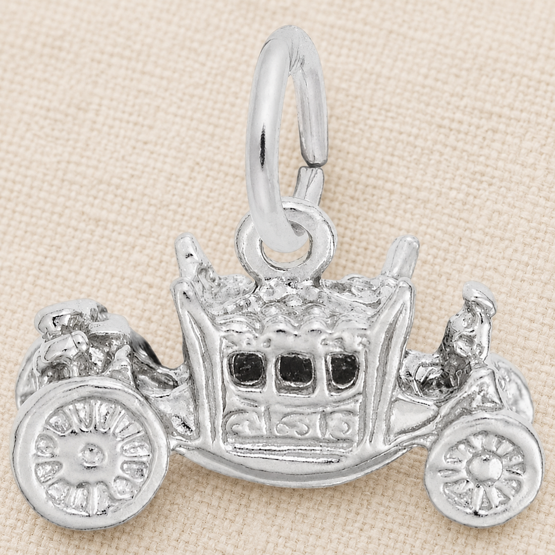 The Rembrandt Charms Royal Carriage Charm—crafted in sterling silver—features an ornate, vintage horse-drawn carriage design with intricate detailing, beautifully displayed on a beige textured background. This exquisite jewelry piece is the perfect fairytale accessory for anyone seeking a regal carriage charm.