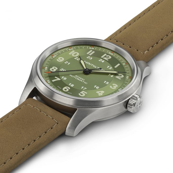 A close-up of the Hamilton Khaki Field Titanium Automatic 42mm wristwatch, showcasing a round, silver-tone stainless steel case and a green dial with Arabic numerals. The watch is equipped with a tan leather strap and features a crown on the right side adorned with the Hamilton logo. The dial also includes a 24-hour clock and displays the words "Khaki Field Titanium.