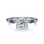 The Gabriel & Co 14K White Gold Round Sapphire and Diamond Engagement Ring features a 2 carat center diamond, marquise-cut blue sapphires on each side, and an ornate band with sparkling diamond accents.