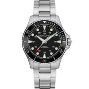 A Hamilton Khaki Navy Scuba Automatic Watch features a 43mm case, silver metal band, black dial with luminous hands and hour markers, date display at the 4 o’clock position, a unidirectional ceramic bezel, and a 24-hour scale.