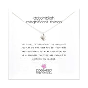 An elegant silver necklace, part of Dogeared's "Accomplish Magnificent Things" collection, features a small starburst pendant. The text above the necklace reads, "Accomplish magnificent things." Below are inspirational words encouraging the wearer to achieve their dreams, proudly attributed to DOGEARED, MADE IN THE U.S.A.