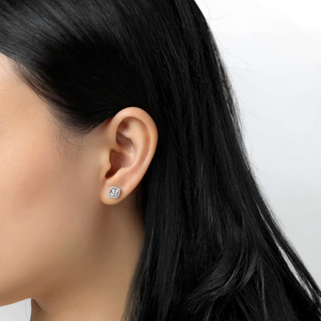 Close-up of a woman's left ear adorned with a sparkling sterling silver stud earring, set against a plain white background. The Cushion Cut Halo Stud Earrings by Lafonn feature a square design with multiple simulated diamonds. The woman's black hair falls smoothly, partially visible in the image.
