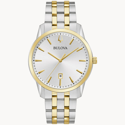 The Bulova Sutton Classic Watch (98B385) by the Bulova Watch Company features a two-tone metal band in silver and gold. It has a round silver watch face with gold hour markers and hands, and includes a date display at the 6 o'clock position. This elegant dress watch is designed with a silver case accented with refined gold details.