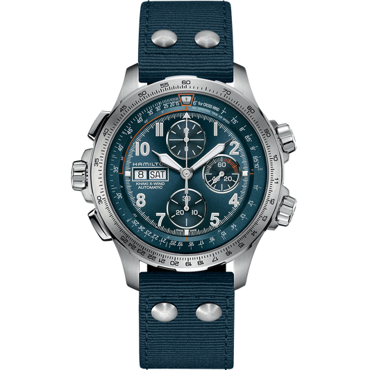 A Hamilton Khaki Aviation X-Wind Automatic Chronograph watch, featuring a silver-toned case and large, detailed face with multiple dials and a date window showing "28" and "SAT." The timepiece includes a blue fabric strap with metallic rivets and a textured band. The background of the image is transparent.