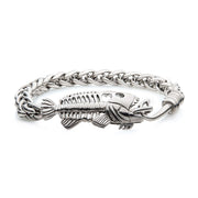The Polished Steel Wheat Chain with Fishbone on Hook Clasp Bracelet by INOX features a detailed fish hook and fish skeleton centerpiece, complete with textured bones and a braided wheat chain link design. The stainless steel bracelet boasts a reflective metallic finish.