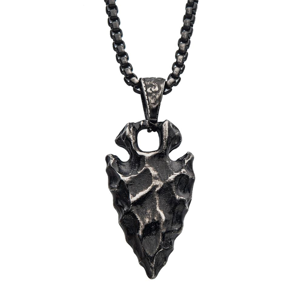 A rugged, dark metal arrowhead pendant with intricate detailing hangs from a thick, textured chain. The INOX men's jewelry piece has an antique finish, accentuating the rough, handcrafted appearance and giving it a rustic and warrior-like charm.