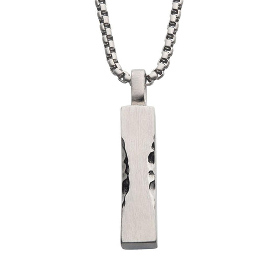 The Matte Steel Chiseled Engravable Drop Pendant from INOX hangs from a silver box chain and features rough, uneven indents that add to its rustic and rugged look. The pendant's matte steel finish complements the medium-length chain perfectly.