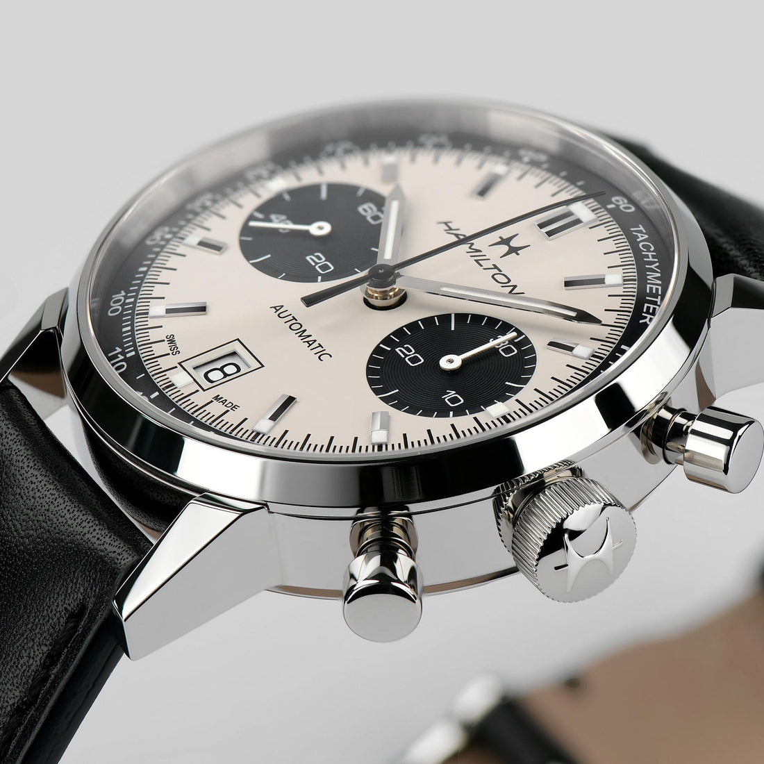 Close-up of a Hamilton Intra-Matic Automatic Chronograph watch featuring a stainless steel case, black leather strap, cream panda dial with black subdials, and a date display at 6 o'clock. The top and side view showcases the intricate design of the crown and push-buttons, highlighting its automatic movement.