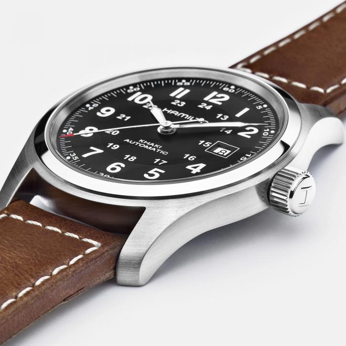 A close-up of the Hamilton Khaki Field Automatic Watch showcases its elegant brown leather strap and sleek silver case. The black dial is driven by the H-10 automatic caliber, offering an impressive 80-hour power reserve, and features Arabic numerals, white minute markers, and a date window at the 3 o'clock position. The watch has white hands and hour markers, along with a crown adorned with an "H" symbol.