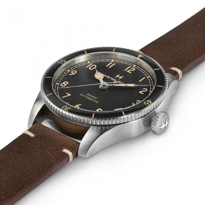 A close-up image of the Hamilton Aviation Pilot Pioneer Automatic Watch | 38mm, featuring a stainless steel case, black dial, and tan leather strap. The watch is designed with Arabic numerals, luminescent hands, and a small window indicating "automatic pilot watch" on the dial. The brand's logo is engraved on the crown.
