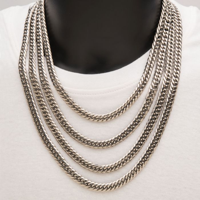A person, obscured from full view, wears an 8mm Steel Dome Curb Chain by INOX over a white garment. The 20" Men's Stainless Steel Necklace showcases thick, interlinked chains that drape in five tiers, creating a bold and stylish contrast against the plain shirt.