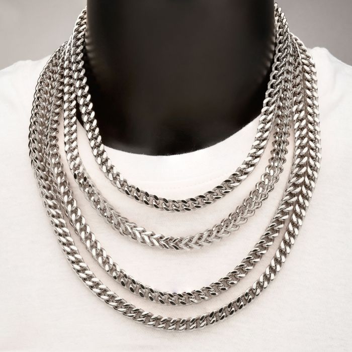 A person adorned with multiple 8mm Steel Franco Chains by INOX around their neck over a white shirt. The men's necklaces from the INOX collection vary in length, creating a cascading effect. The neutral background enhances the shine and intricate links of the 20" Franco chains.