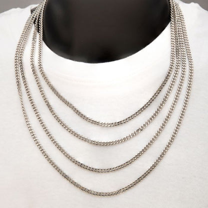 A display of the 4mm Steel Diamond Cut Curb Chain Necklace by INOX, draped around a black mannequin wearing a white top. The 22" men's stainless steel necklace, consisting of four Diamond Cut Curb Chains arranged one above the other, creates a striking layered effect.