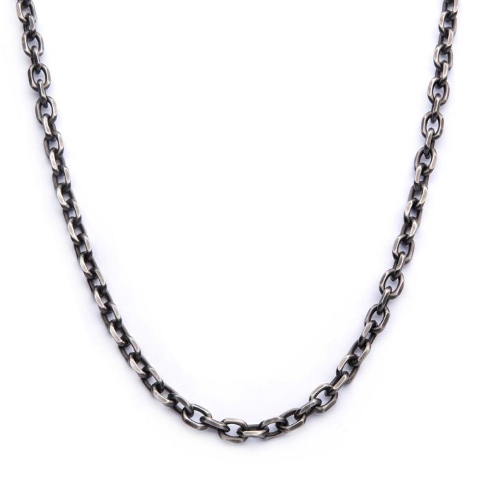 A close-up view of a 7mm Oxidized Steel Knife Edge Link Chain | 24" | INOX forming a semicircle. The knife edge link chain is uniformly oval-shaped and interlocked, with a slightly distressed finish, giving it a rugged, vintage appearance. The background is plain white.