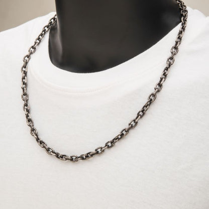 A close-up image of a person wearing a white T-shirt and an INOX 7mm Oxidized Steel Knife Edge Link Chain | 24". The focus is on the 24 inch necklace draped elegantly around the neck, while the background remains blurred and neutral.