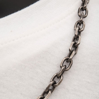 Close-up of a 24 inch necklace resting on a white fabric, likely a shirt. The 7mm Oxidized Steel Knife Edge Link Chain | 24" | INOX has oval links with a slightly textured surface. The white fabric underneath is smooth and appears to be cotton.